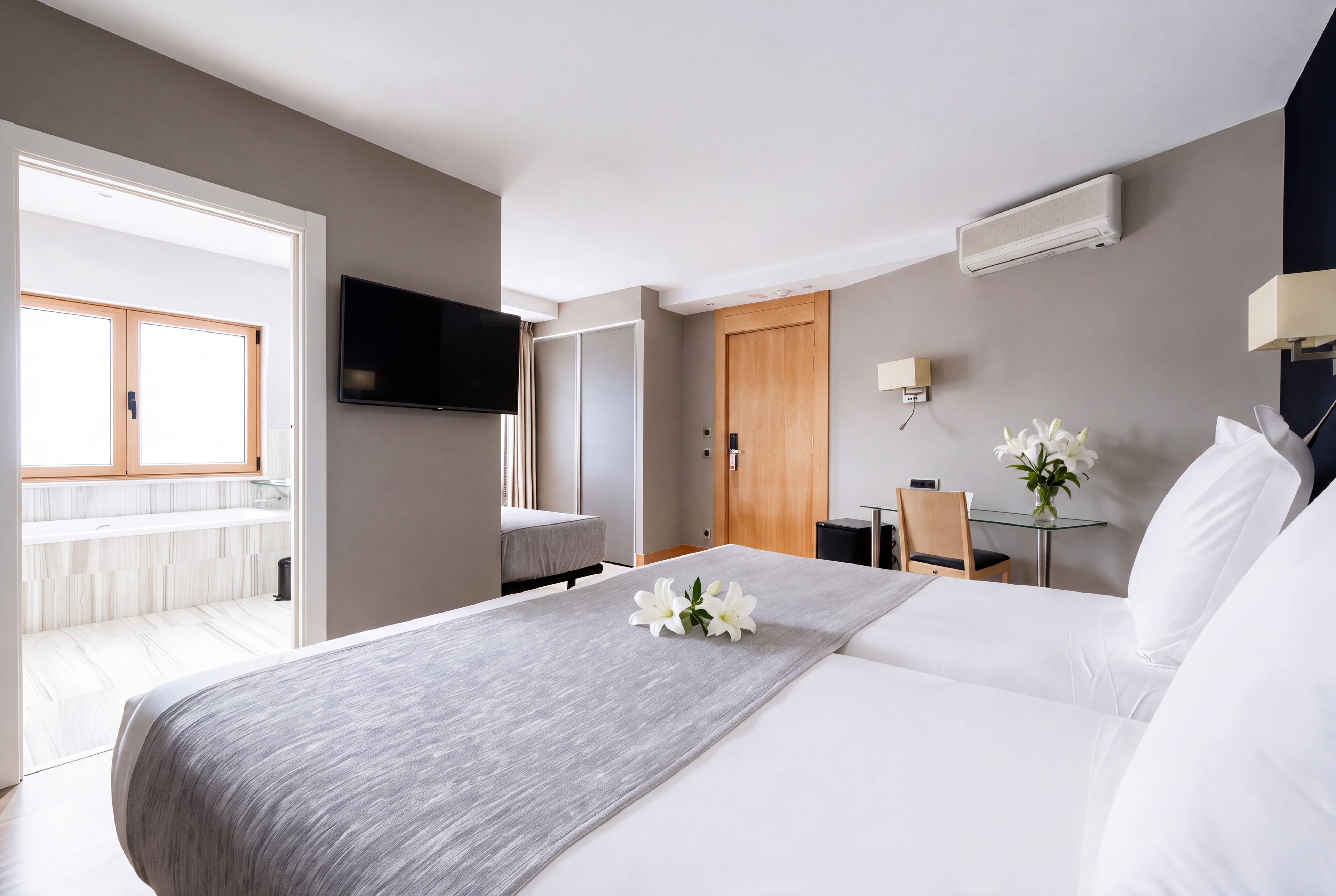 A hotel room with a bed, a desk, a television, and a bathroom visible through an open door.