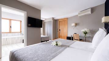 A hotel room with a bed, a desk, a television, and a bathroom visible through an open door.