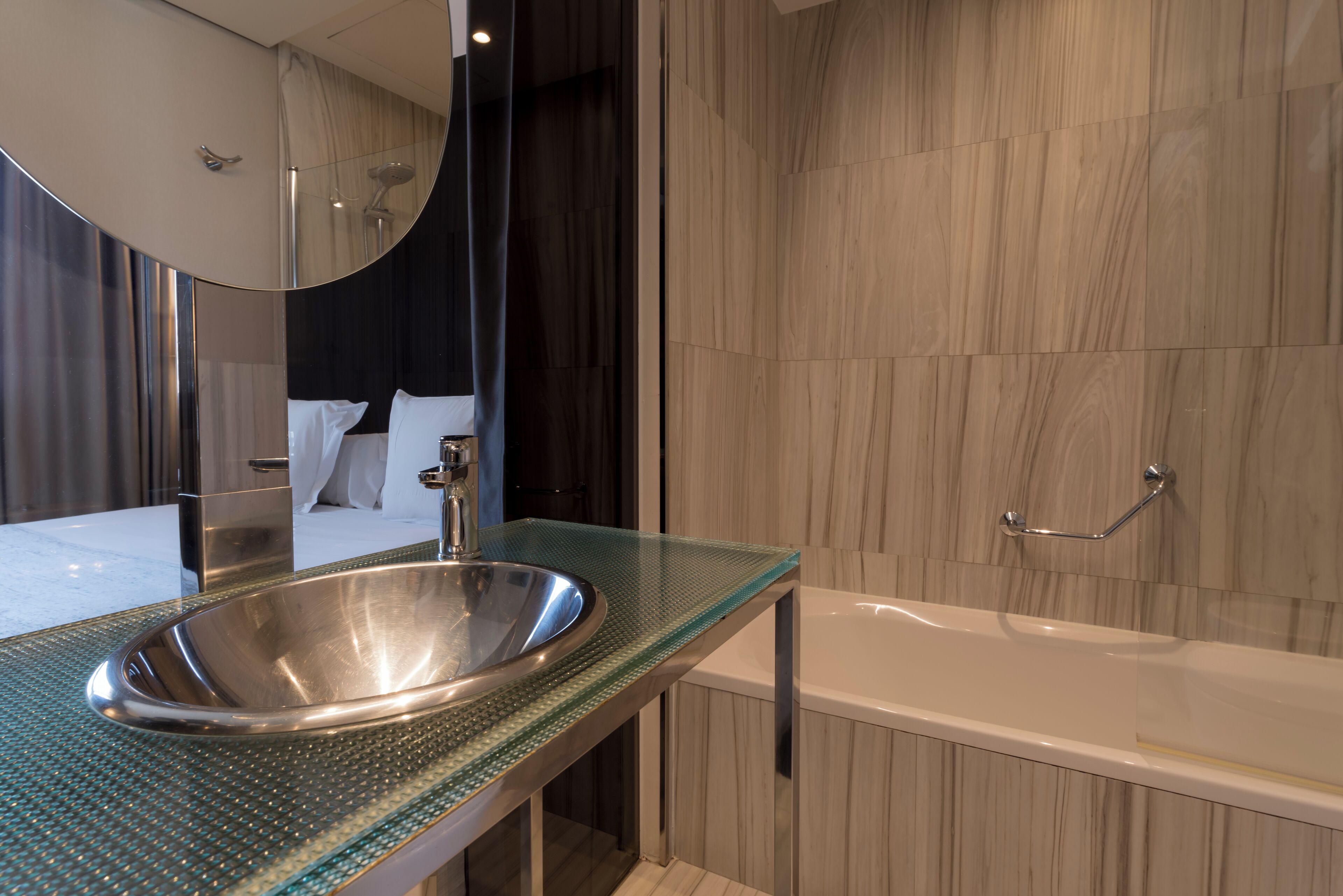 A modern bathroom with a glass-topped sink, a large mirror, a bathtub, and wooden wall panels.