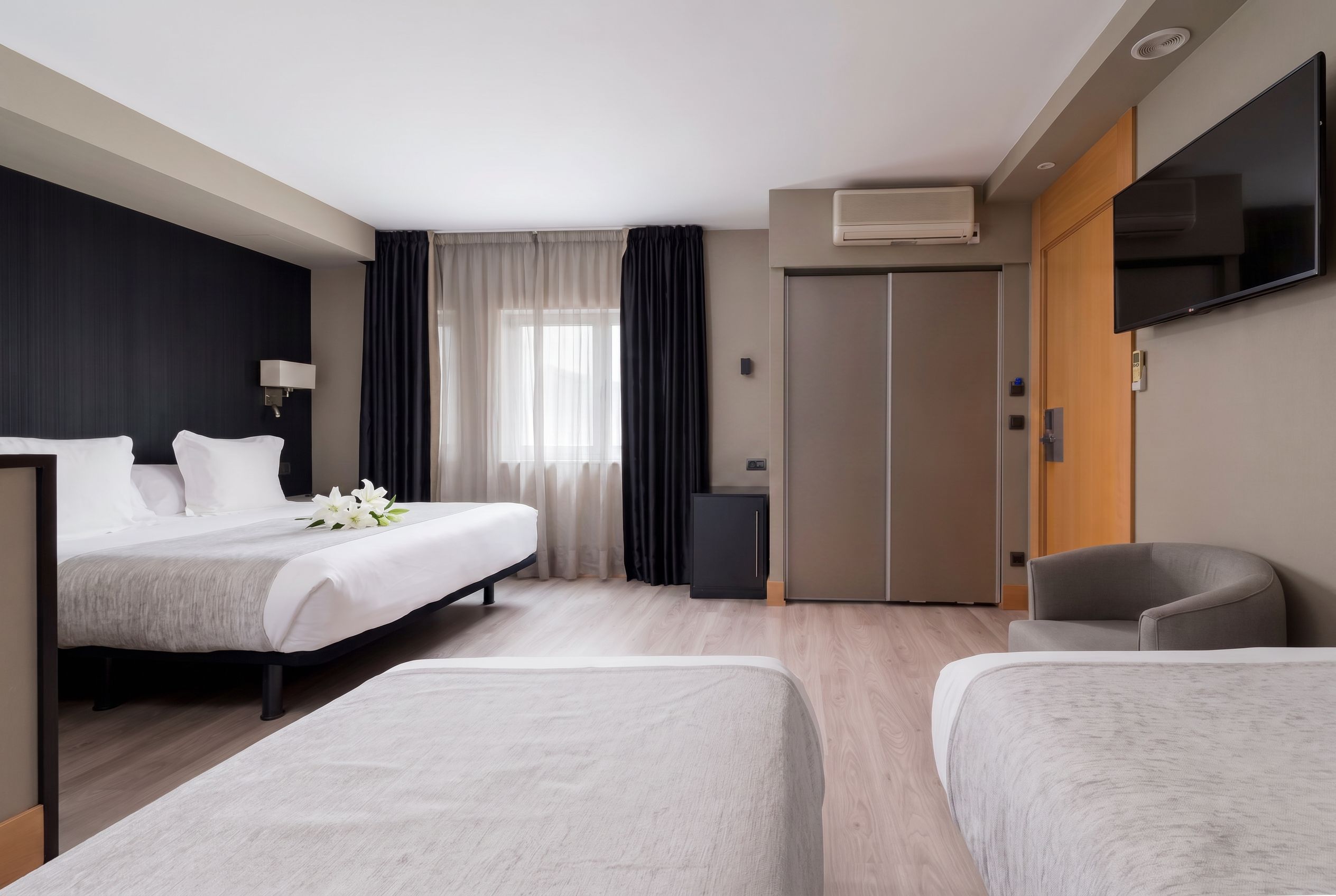 A hotel room with a bed, a desk, a chair, a wardrobe, and a TV.