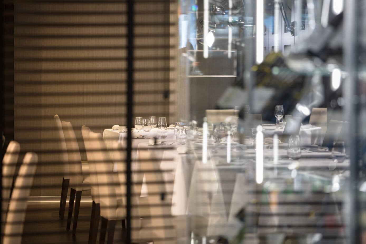 Comedor con mesas dispuestas para comer, sillas y un divisor de vidrio reflectante.