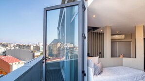 Una camera da letto moderna con un balcone in vetro, un letto con biancheria bianca e vista sulla città.
