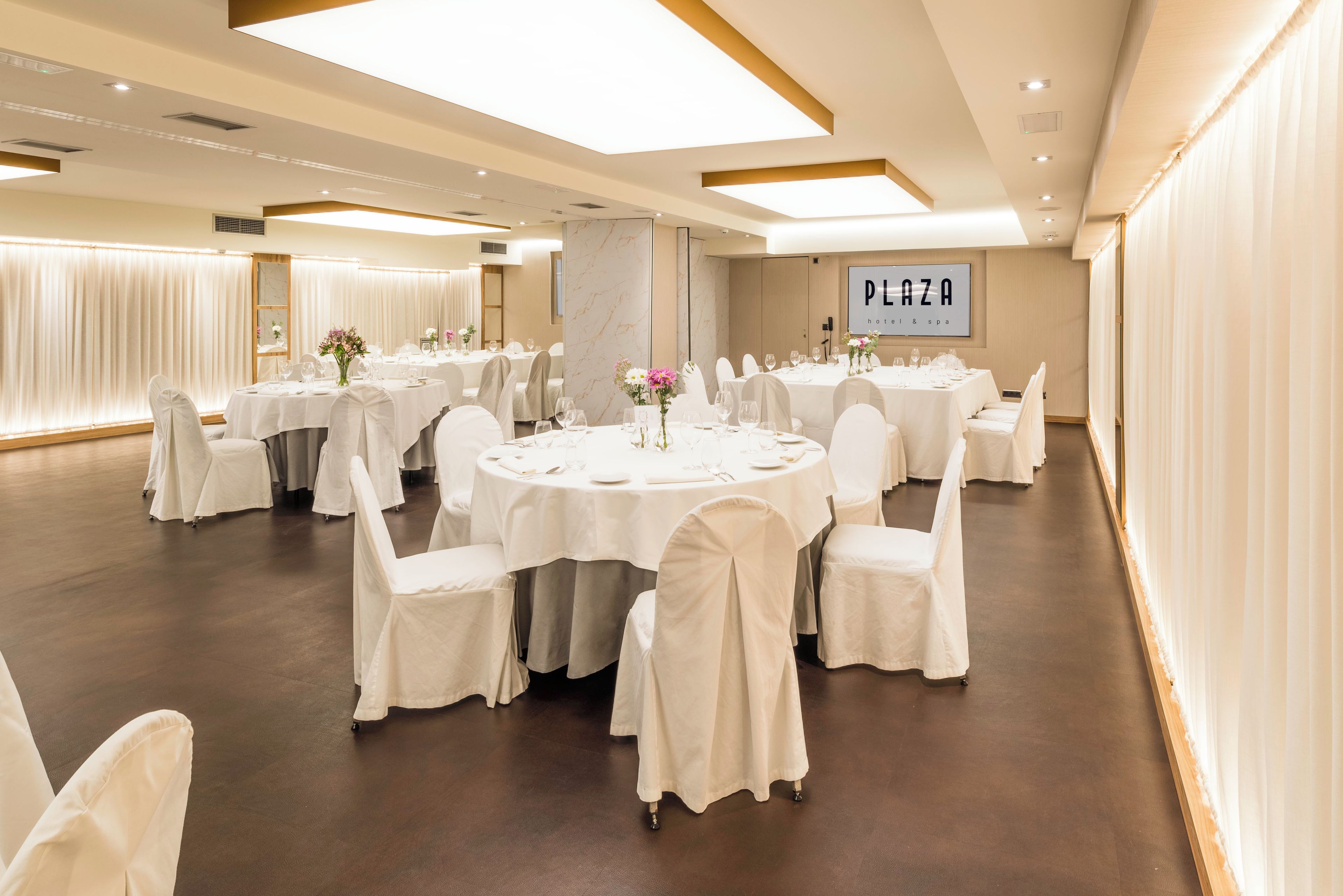 A banquet hall with round tables, white chairs, and a large sign on the wall.