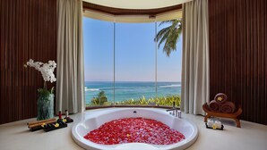 Un baño con una bañera llena de pétalos de rosa, un jarrón con flores blancas y un atril de madera con toallas.