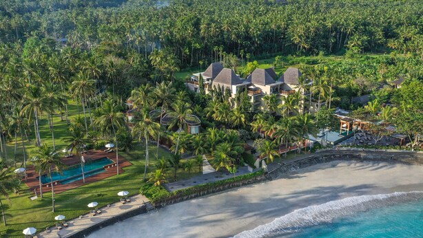 Vista aérea de un resort con varias construcciones, una piscina y acceso a la playa.