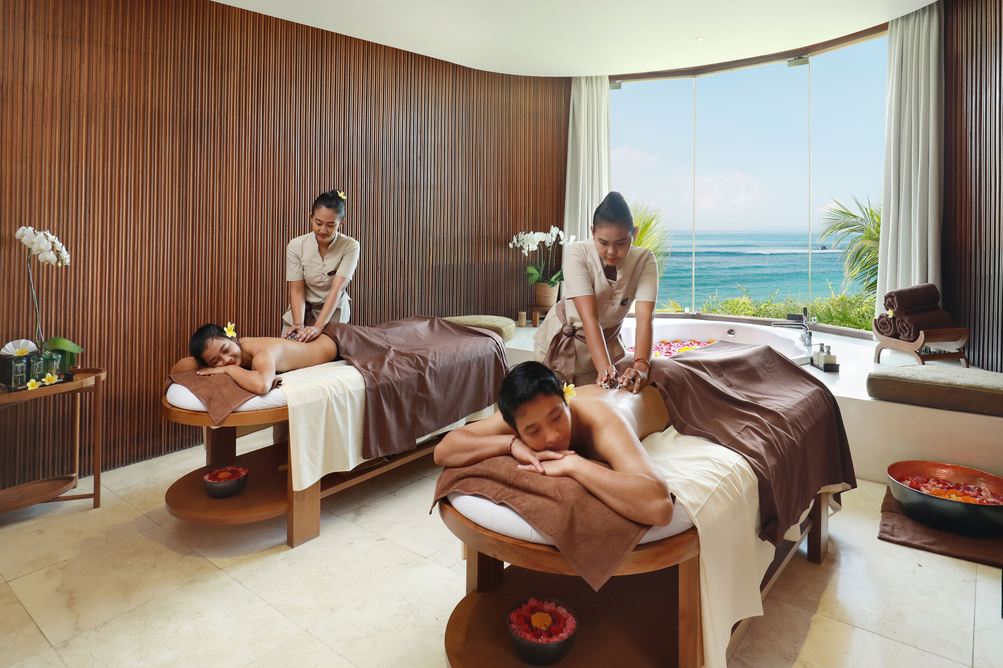 Una stanza spa con due lettini da massaggio, un'ampia finestra vista oceano e una parete in legno.