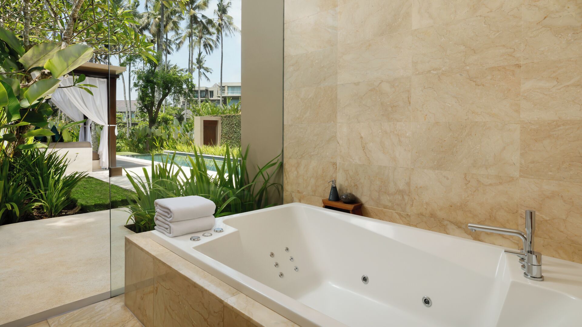 Ein modernes Badezimmer mit einer großen Badewanne, Marmorwänden und Blick auf einen Pool und Grünflächen.