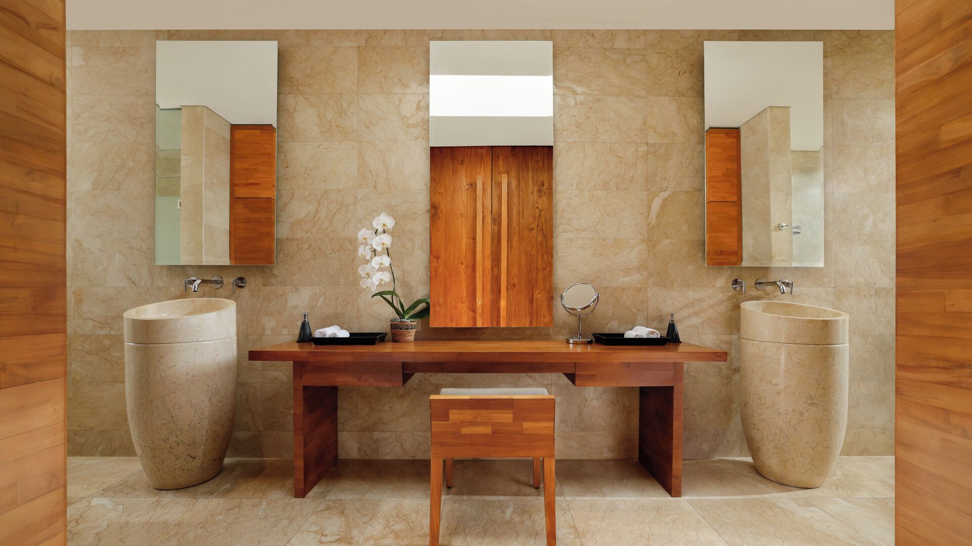 A bathroom with two sinks, a wooden vanity, a mirror, and a potted orchid.
