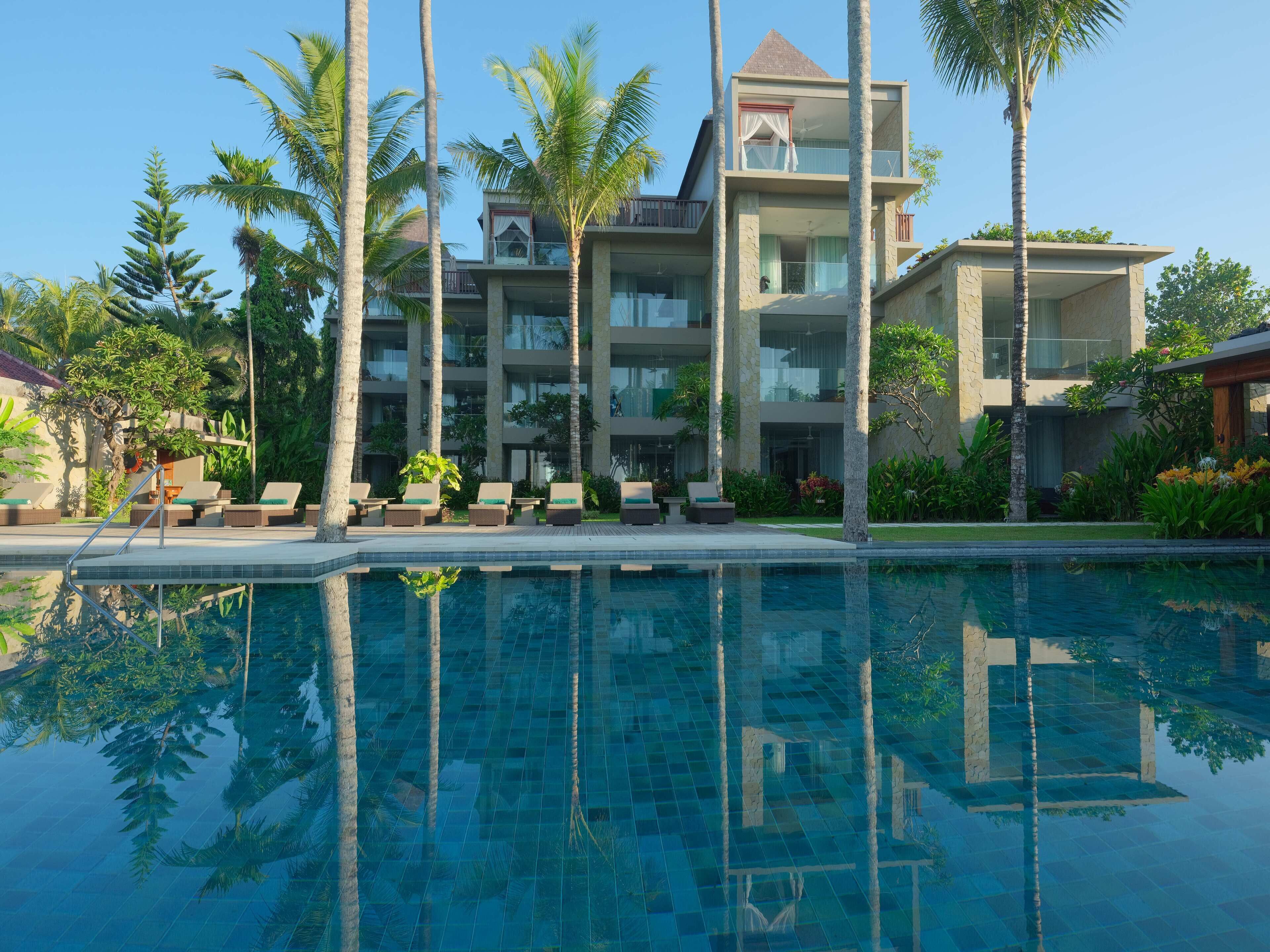 Un resort con piscina, palmeras y un edificio de varios pisos con balcones.
