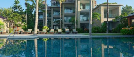 Un resort con piscina, palmeras y un edificio de varios pisos con balcones.