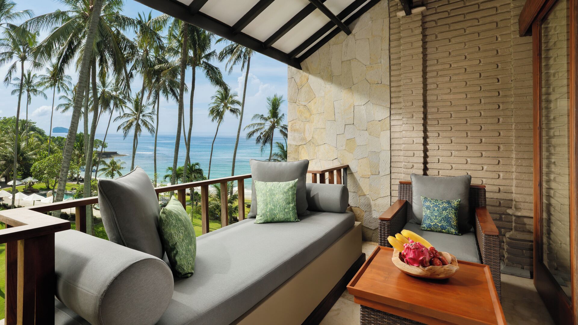 A balcony with a sofa, cushions, and a table with fruit.