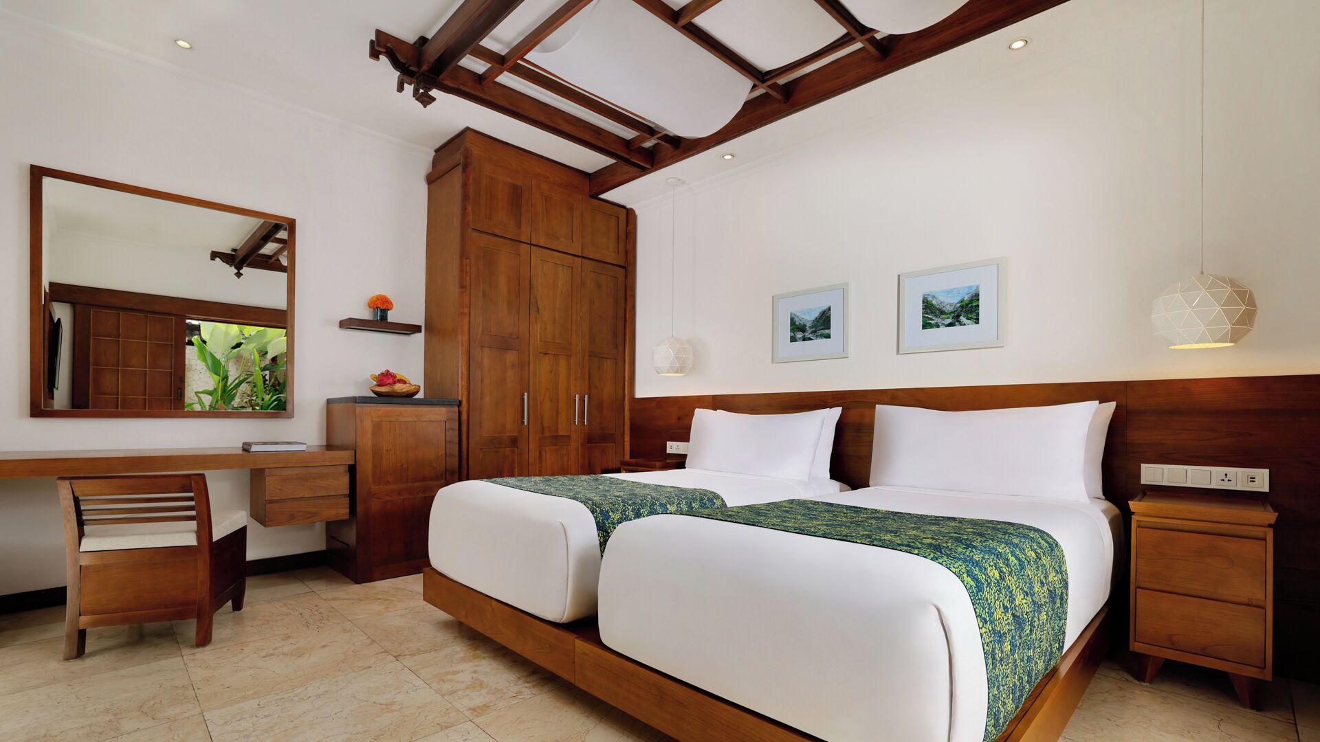 A bedroom with a wooden headboard, two beds, a desk, a chair, a wardrobe, and two framed pictures on the wall.