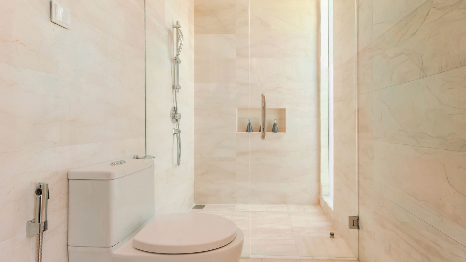 Un baño moderno con inodoro, ducha y zona de ducha con mampara de vidrio.