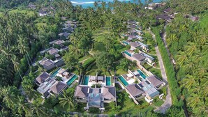Vista aérea de un complejo turístico con varias cabañas, piscinas y exuberante vegetación tropical.