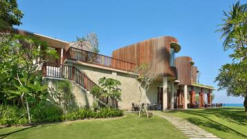 A modern resort with a stone facade, a covered outdoor dining area, and a view of the ocean.