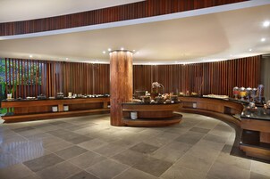 Un espace d’accueil moderne avec un comptoir en bois aux lignes courbes, un pilier central et un sol carrelé.