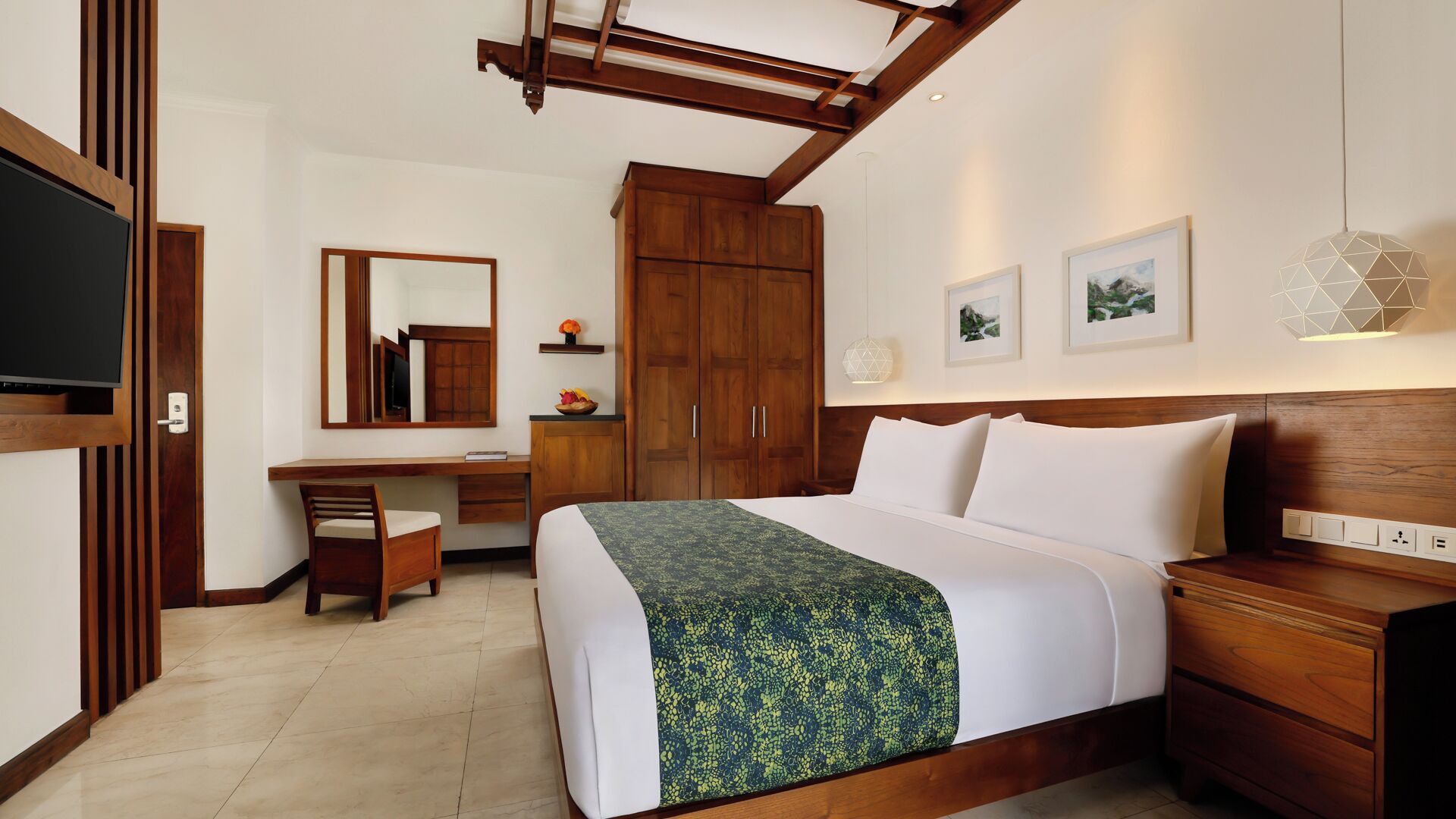 A hotel room with a bed, a desk, a chair, a wardrobe, a television, and artwork on the wall.