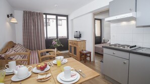 A compact room with a dining table set for breakfast, a kitchenette, a bed with checkered bedding, and a window with curtains. - Résidence le Rond Point des Pistes (Tignes)