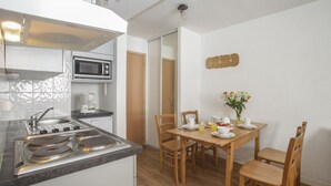 A compact kitchen with a stove, microwave, and sink. There is a dining table with chairs and a vase of flowers. - Résidence le Rond Point des Pistes (Tignes)