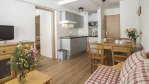 A compact living space with a kitchenette, a dining area, and a seating area with a checkered sofa. - Résidence le Rond Point des Pistes (Tignes)