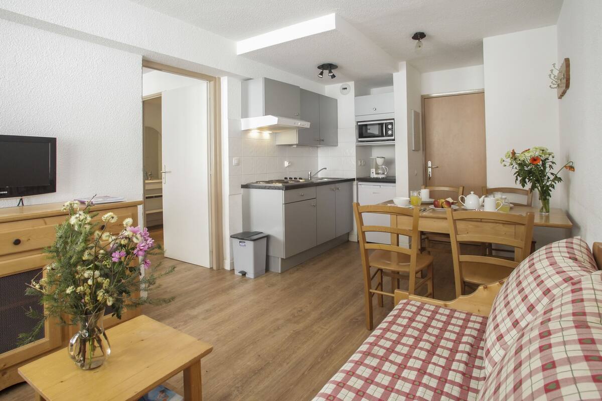 A compact living space with a kitchenette, a dining area, and a seating area with a checkered sofa.