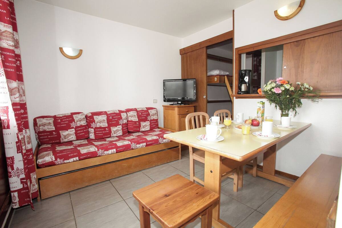 Ein kompakter Wohnbereich mit einer Couch, einem Esstisch mit Stühlen, einem Fernseher und einem Schrank.