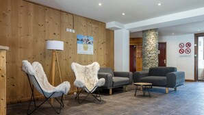 A lobby with wooden panel walls, a stone pillar, and a grey sofa. - Odalys Residence le hameau du Borsat (Tignes)