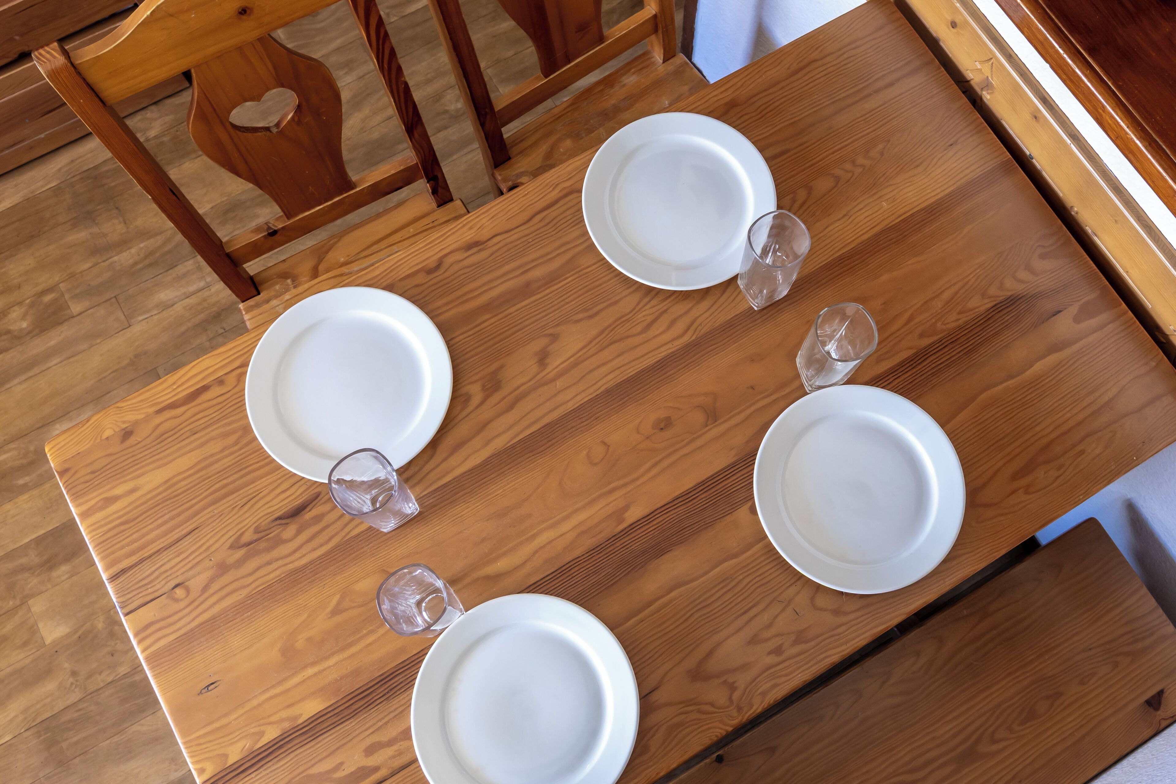 A wooden dining table with four white plates and two clear glasses.