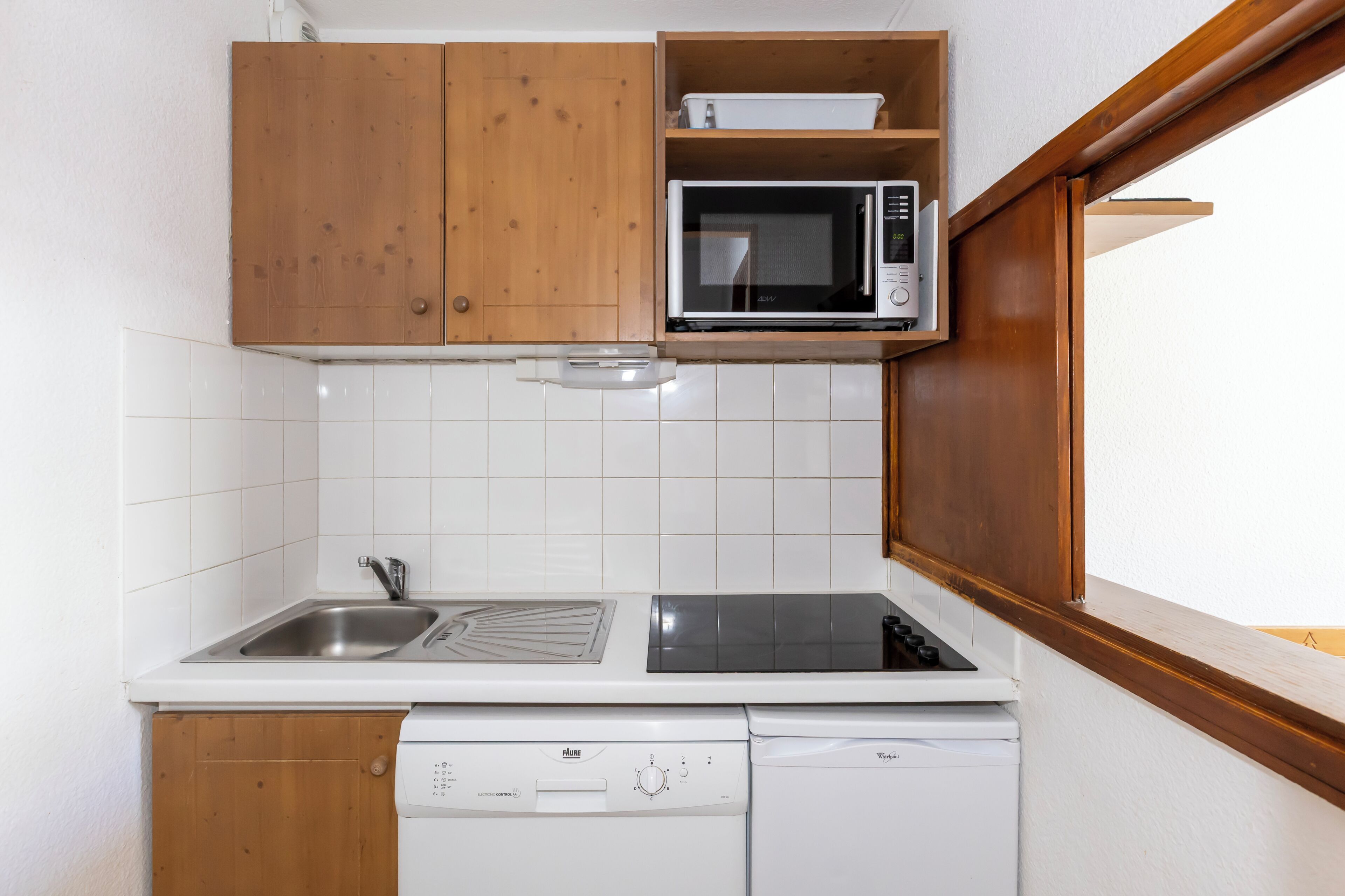 Een kleine keuken met houten kastjes, een magnetron, een spoelbak en een vaatwasser.