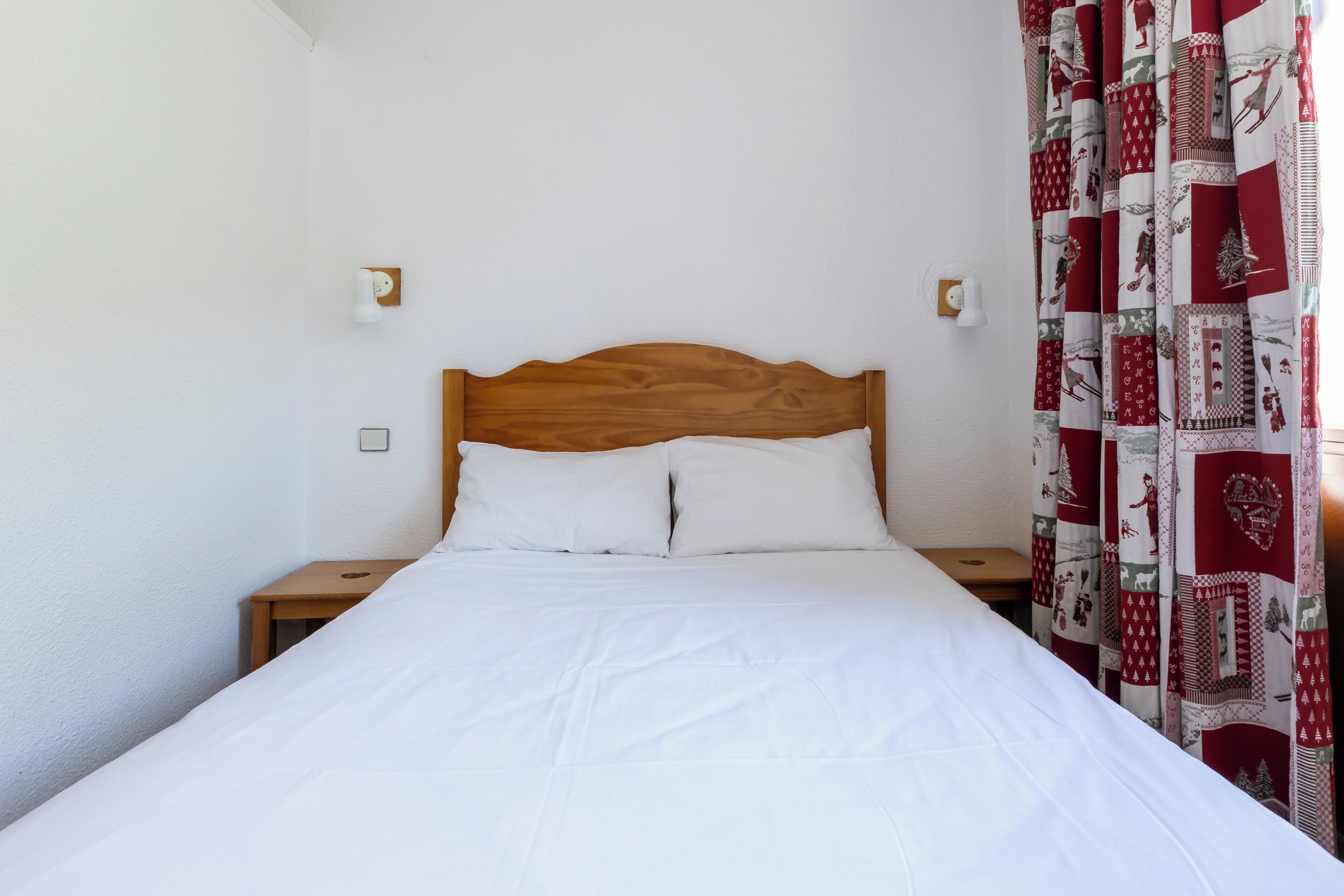A bed with a wooden headboard, white bedding, two bedside tables, and a patterned curtain.