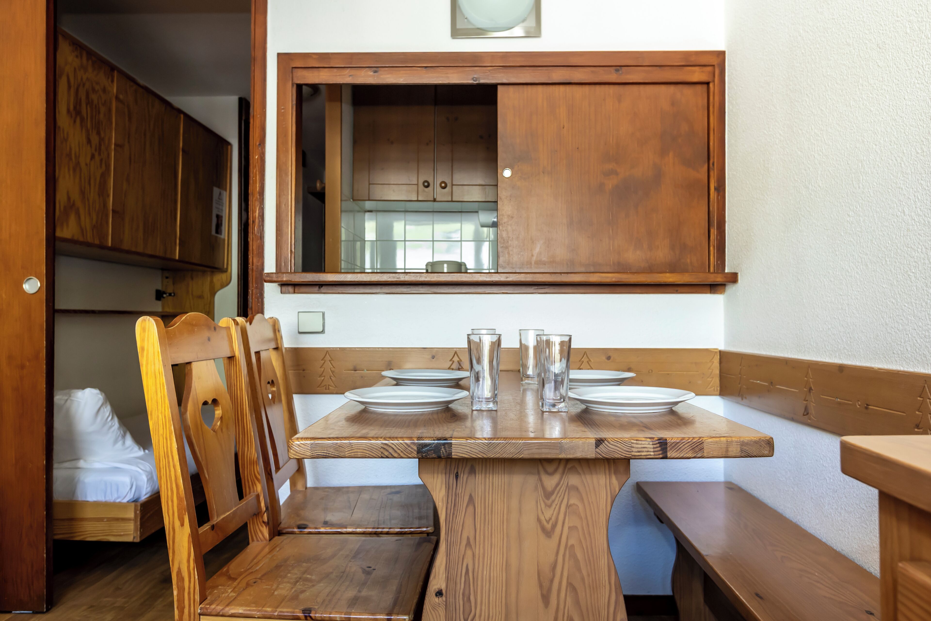 Une cuisine compacte avec des meubles en bois, une table à manger dressée avec des assiettes et des verres, et un banc.