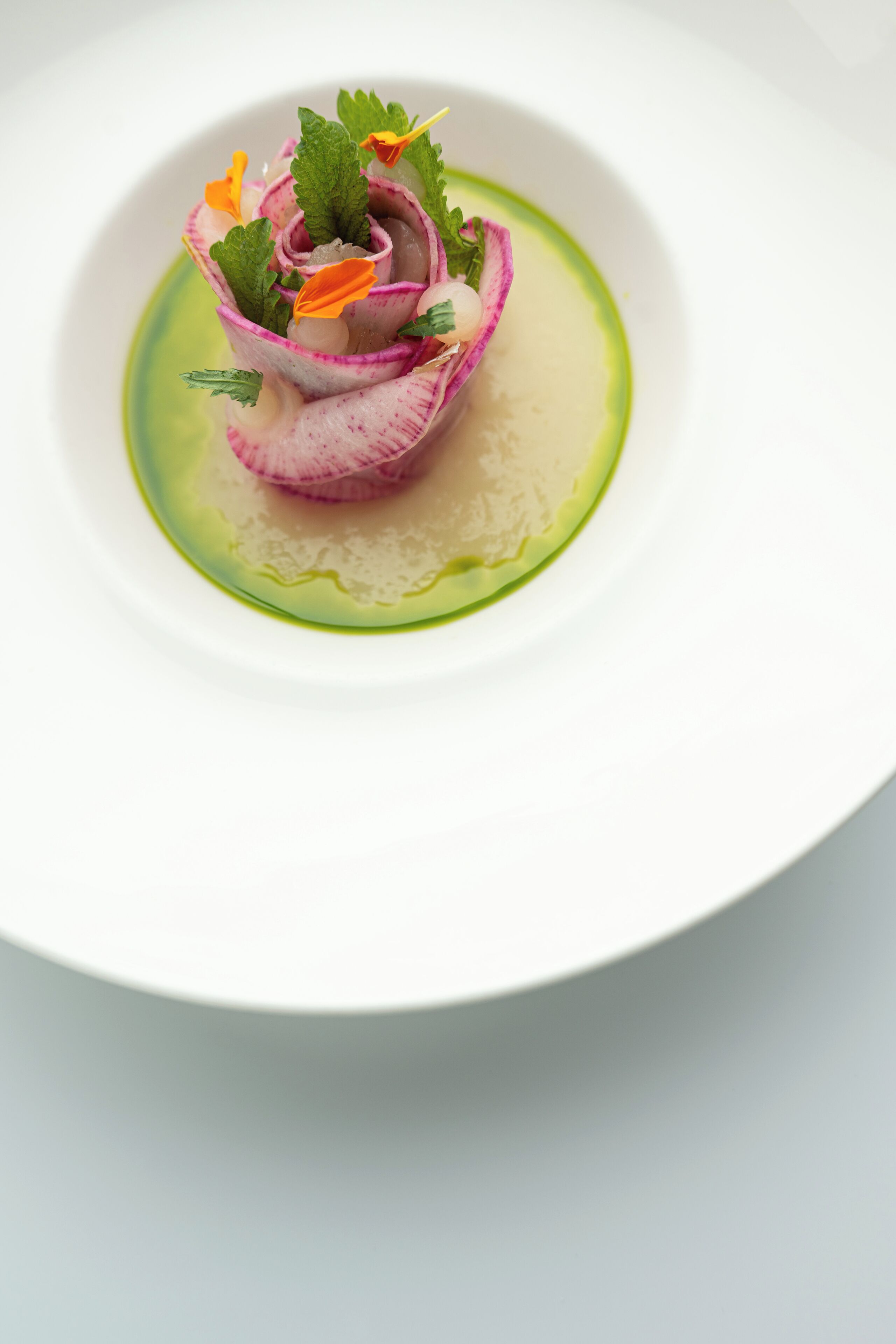 A white plate with a pink and white flower arrangement and green sauce.