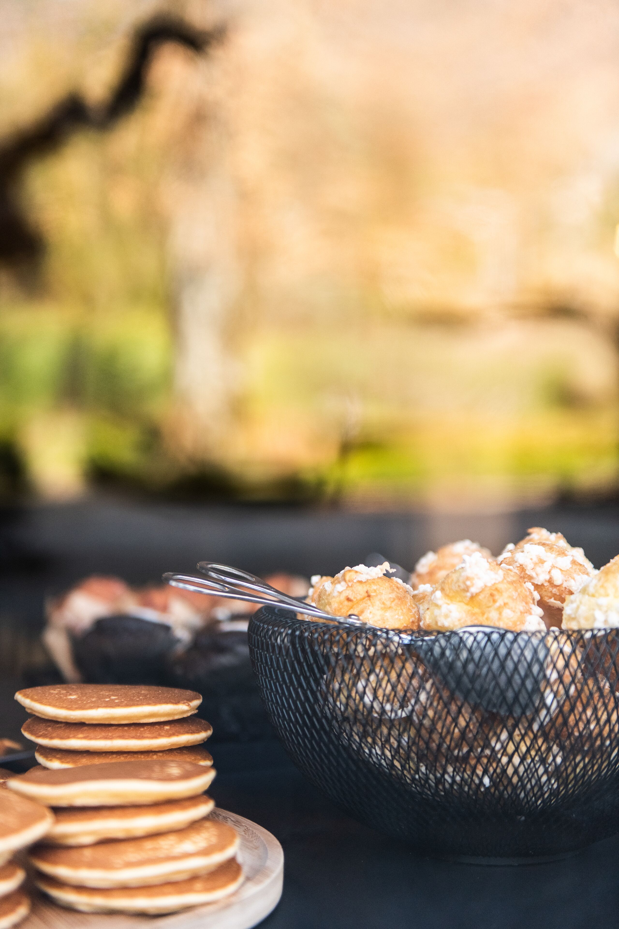 A stack of pancakes and a basket of pastries on a table.