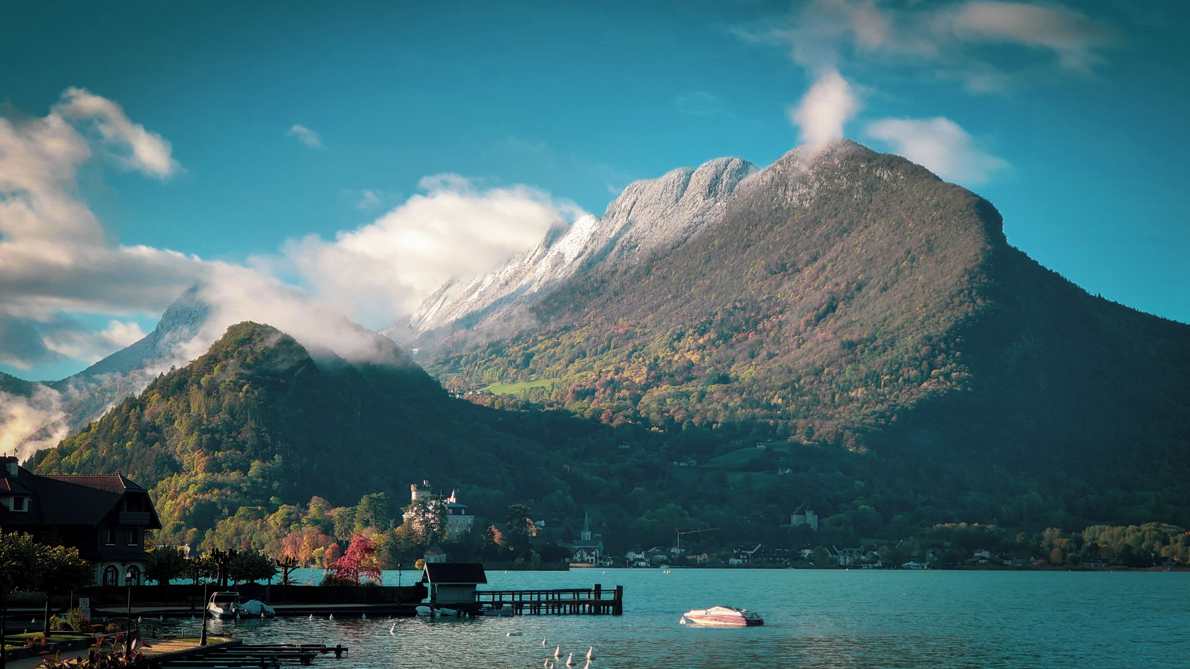 Une montagne surmontée d’un château, un lac et un quai où sont amarrés des bateaux.
