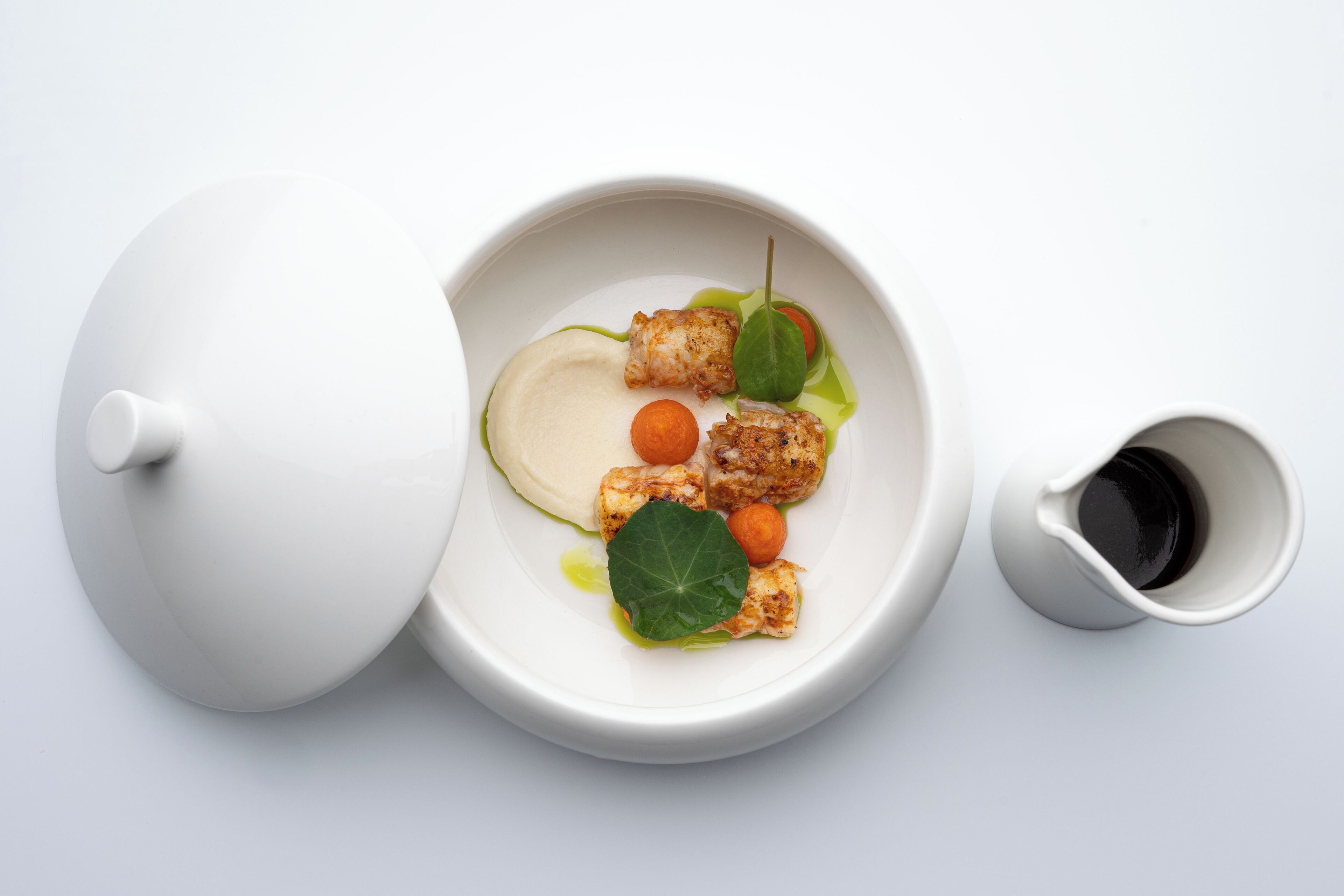 A white teapot and cup on a white surface.