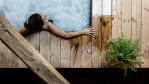 Una persona apoyada en una pared de madera cerca de una bañera de hidromasaje.