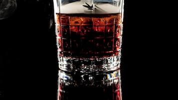 A glass of whiskey with a smoking glass on top, set against a dark background.