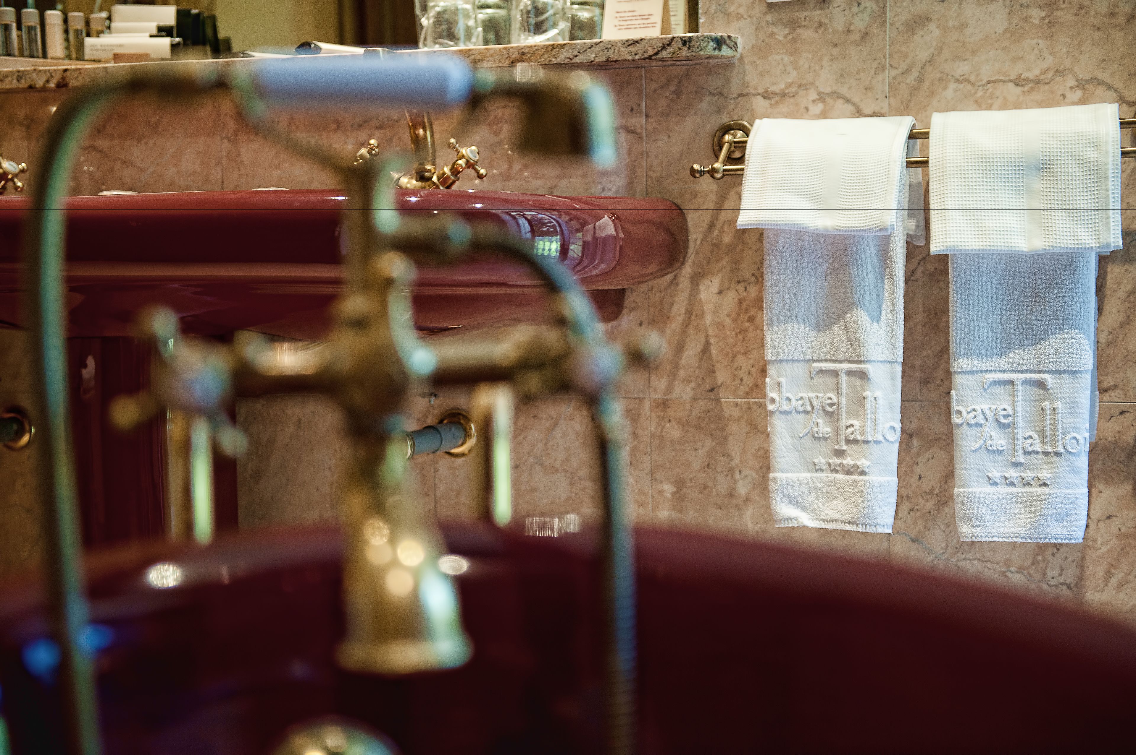 A bathroom with a marble sink, a gold faucet, and two towels hanging on a towel rack.
