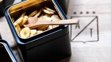 Multiple containers with wooden spoons, one containing sliced bananas and another with nuts.