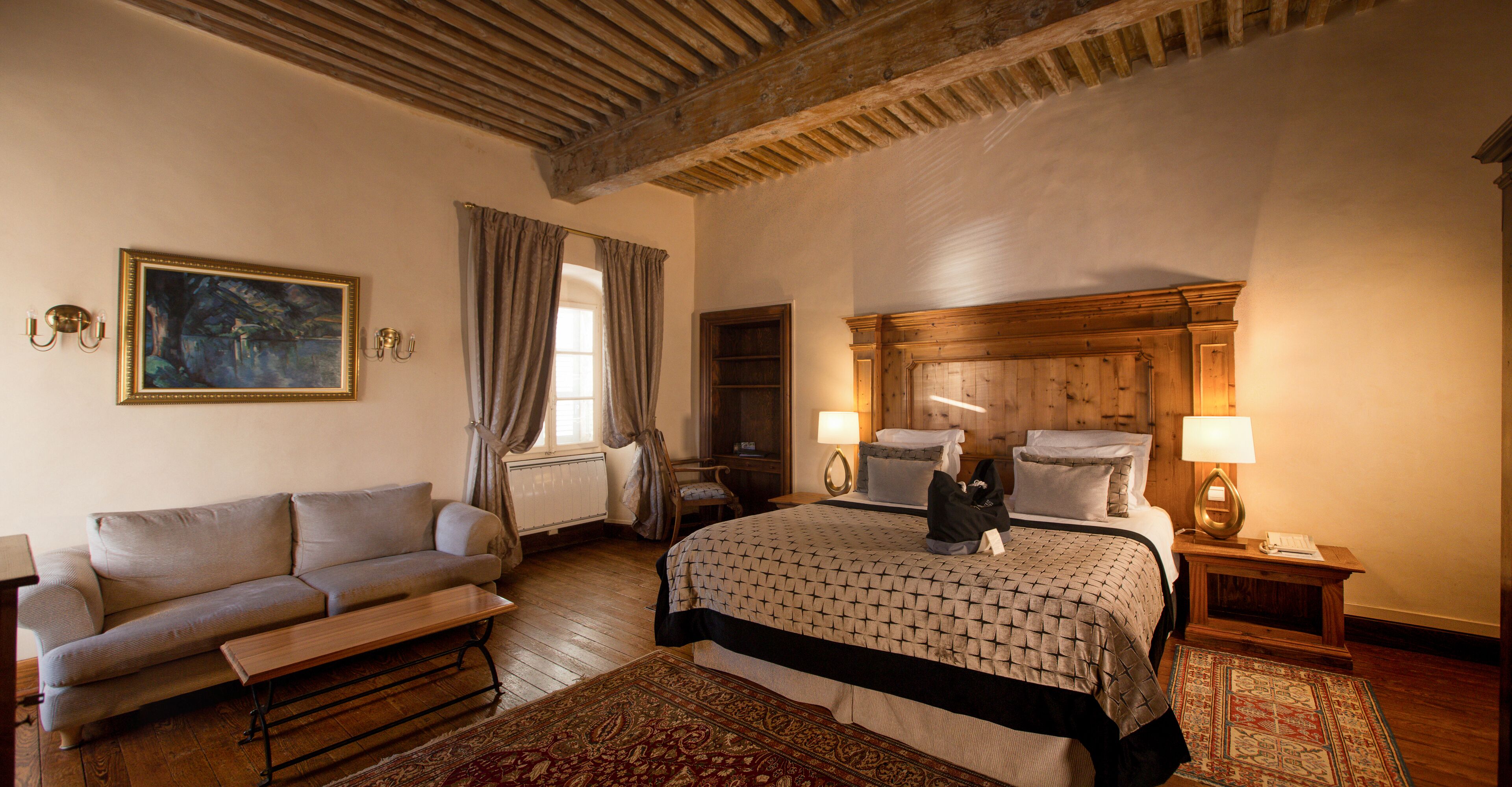 Een slaapkamer met een bed, een slaapbank, een houten hoofdbord, een nachtkastje en een schilderij aan de muur.