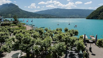 A lakeside view with boats, trees, and mountains.