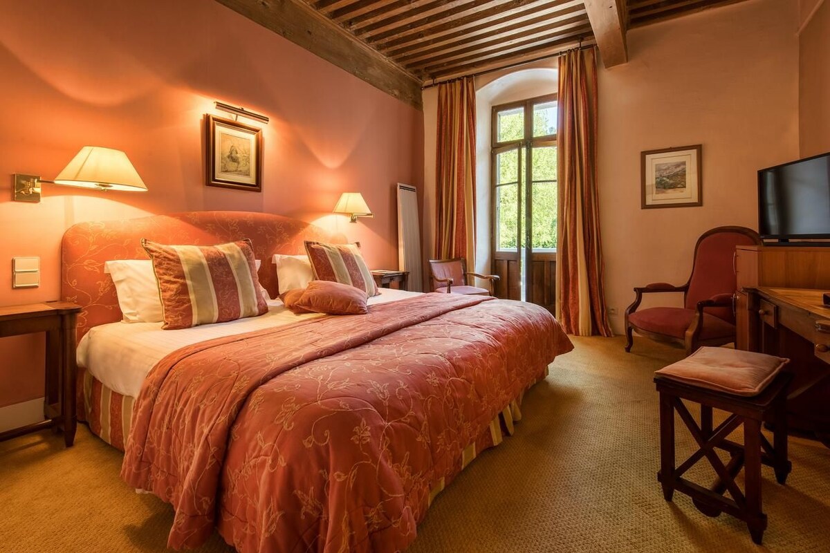 A cozy bedroom with a large bed, two bedside lamps, a television, and a window with curtains.