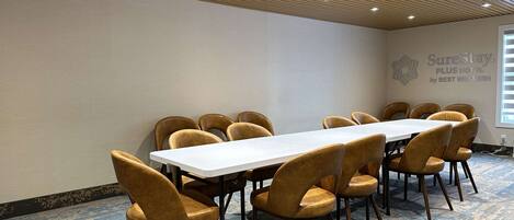 A conference room with a long table and chairs, a wooden ceiling with recessed lighting, and a logo on the wall.