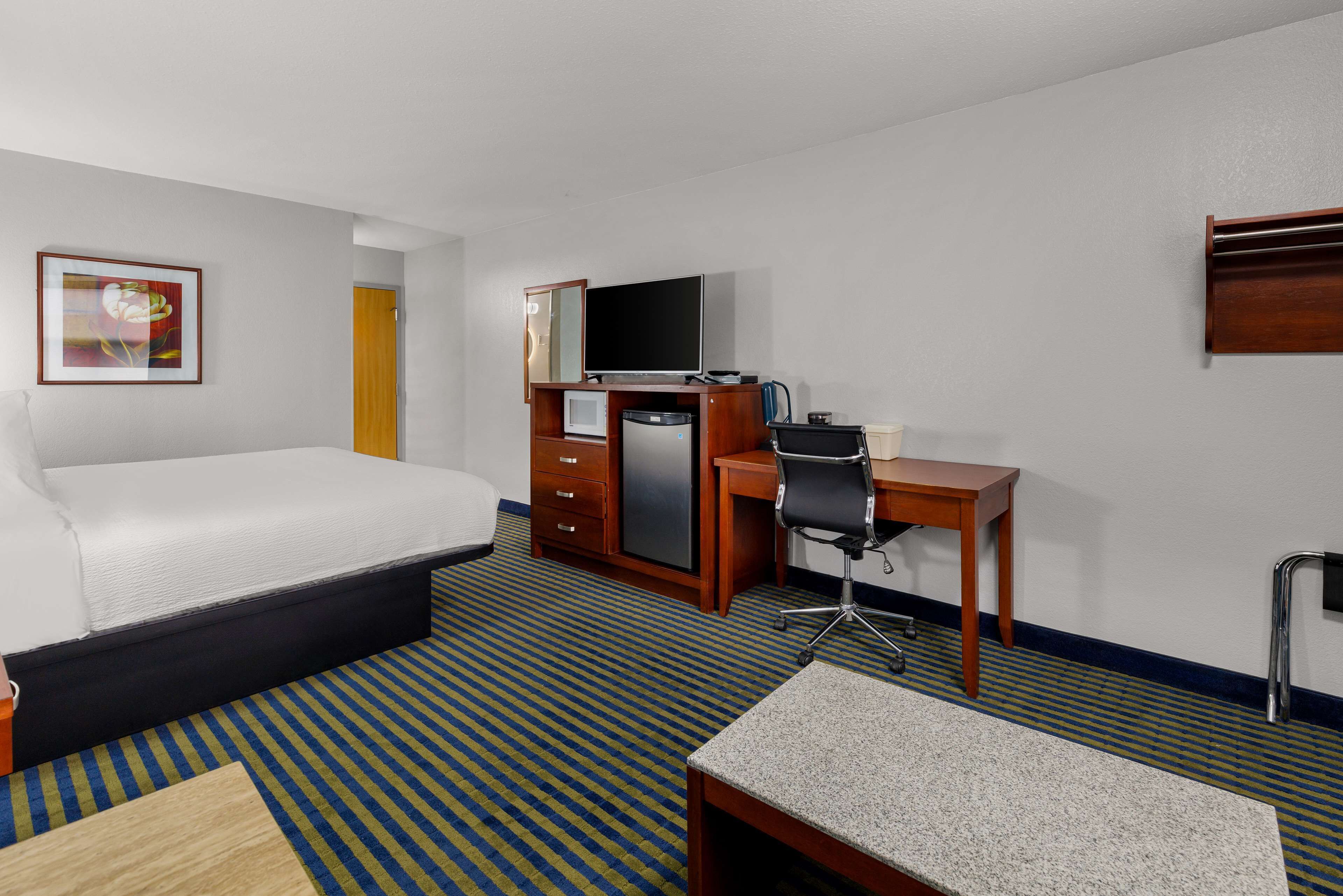 A hotel room with a bed, desk, chair, and a television.