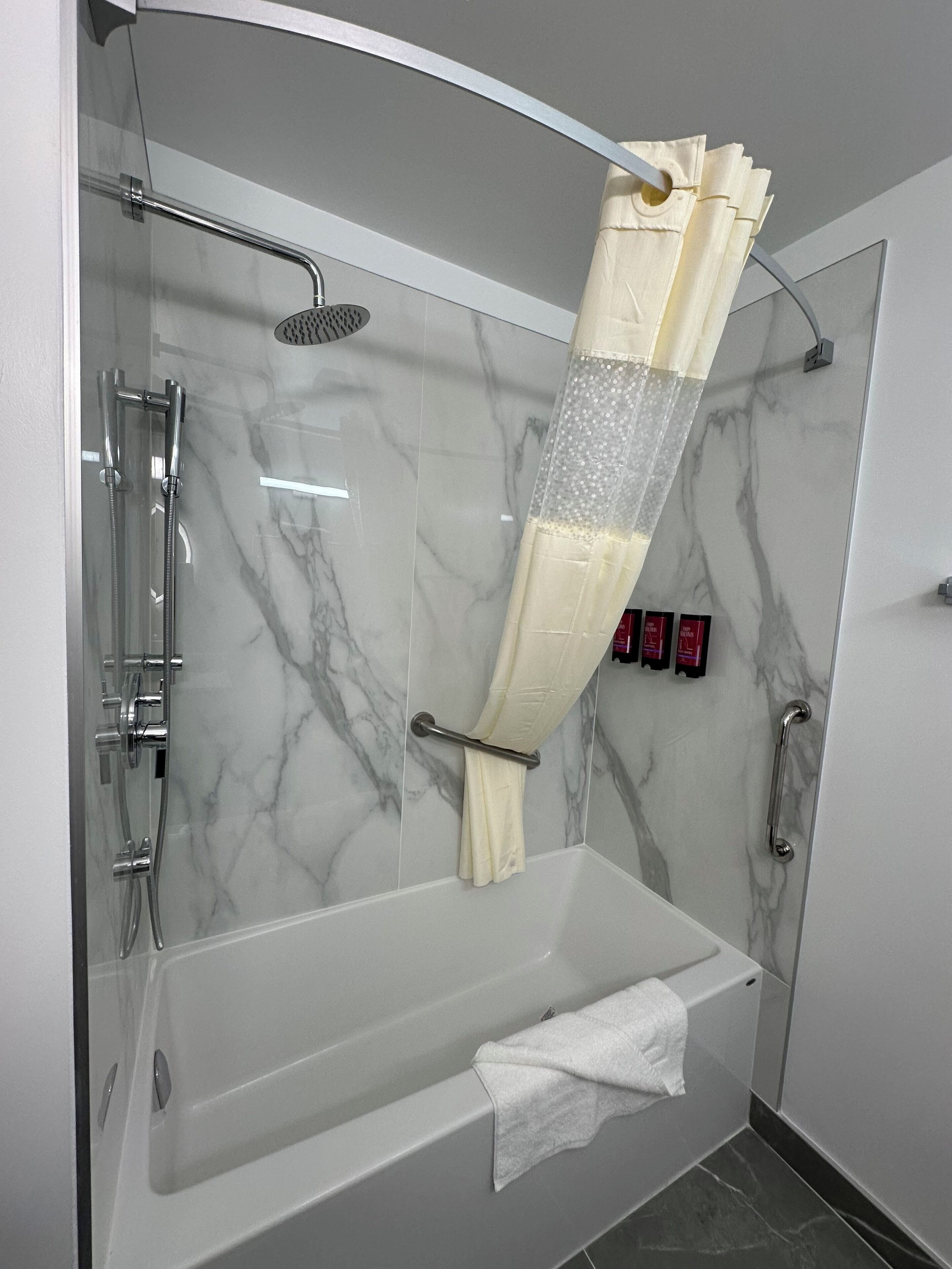 A modern bathroom with a glass-enclosed shower, marble walls, and a white bathtub.