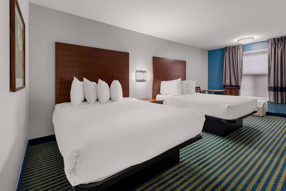 Ein Hotelzimmer mit zwei Betten, einem kleinen Tisch, einem Sessel und einem Fenster mit Vorhängen.