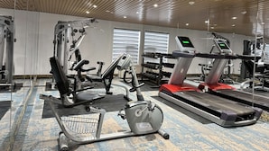Un gimnasio con diversos equipos de ejercicio, incluyendo una cinta de correr, elíptica y máquinas de pesas.