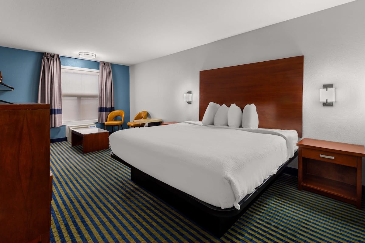 Ein Hotelzimmer mit einem großen Bett, einem hölzernen Kopfteil, einem Schreibtisch, einem Stuhl und einem Nachttisch.