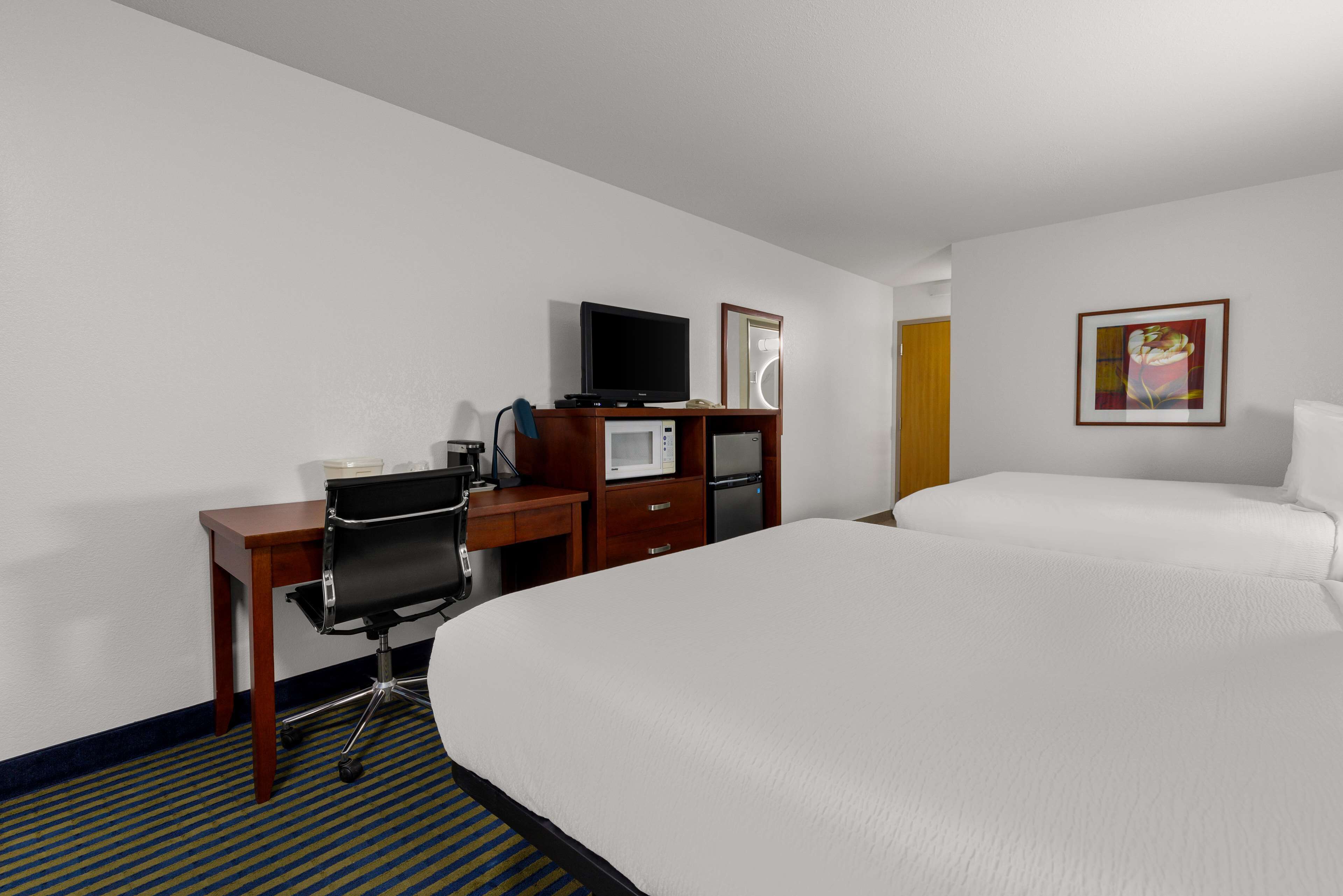 Una habitación de hotel con cama, escritorio con computadora, televisión, microondas y refrigerador.