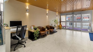 Un área de recepción con techo de madera, un mostrador de recepción, dos sillones de cuero, un televisor y un jarrón grande.